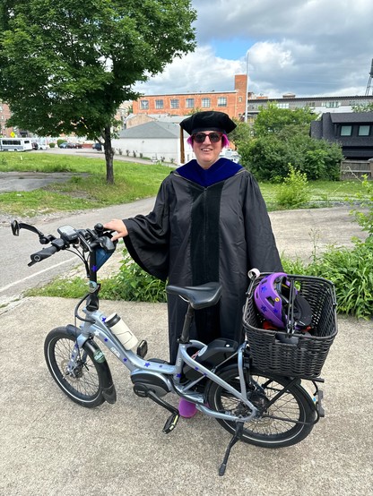 Person wearing academic robes and standing next to a bike