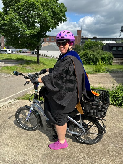 Person wearing academic robes and a helmet on a bike