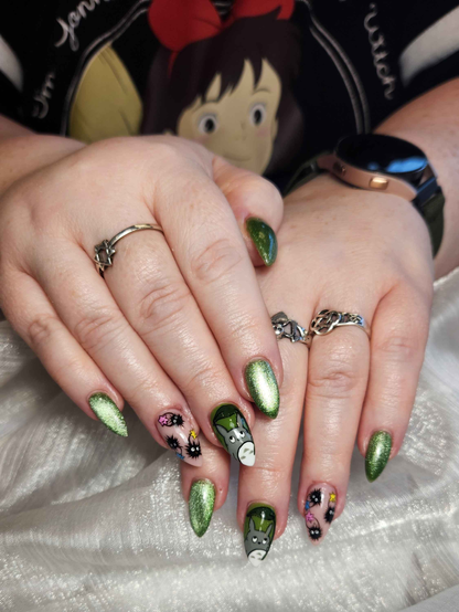 My hands showing off my nails. Three nails on each hand hare sparkly green. One nail has totoro with a leaf umbrella, the other nail has three soot sprites.