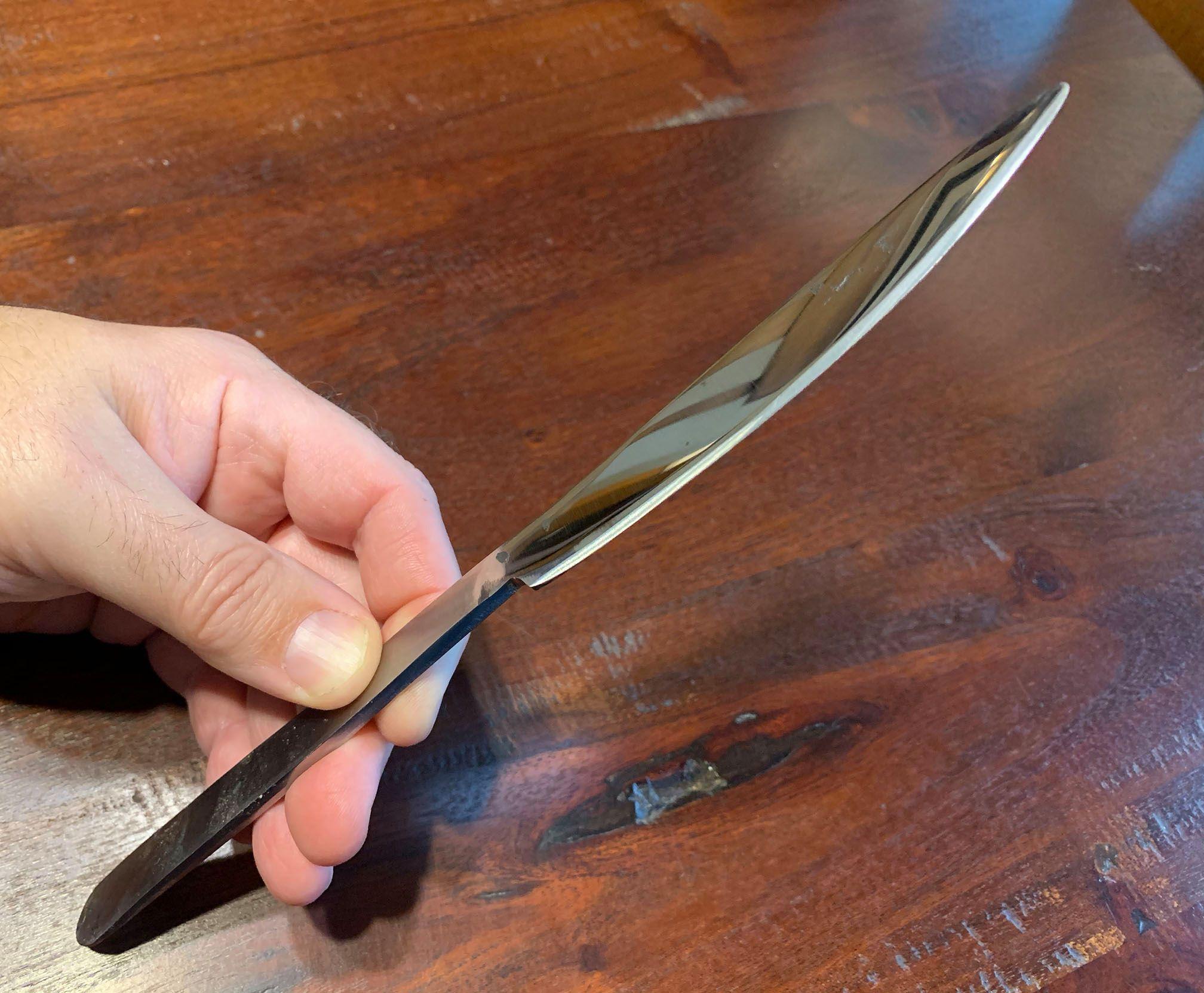 A hand-forged table knife, held by a hand. The blade has been ground, sharpened and given a high polish.
